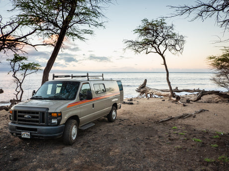 Tan RV rental van parked on a serene Hawaiian beach at dawn, offering tranquil ocean views for your coastal adventure.