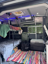 Step inside this RV rental's cozy interior, featuring bunk beds, a vibrant rag rug, and a Dometic cooler.