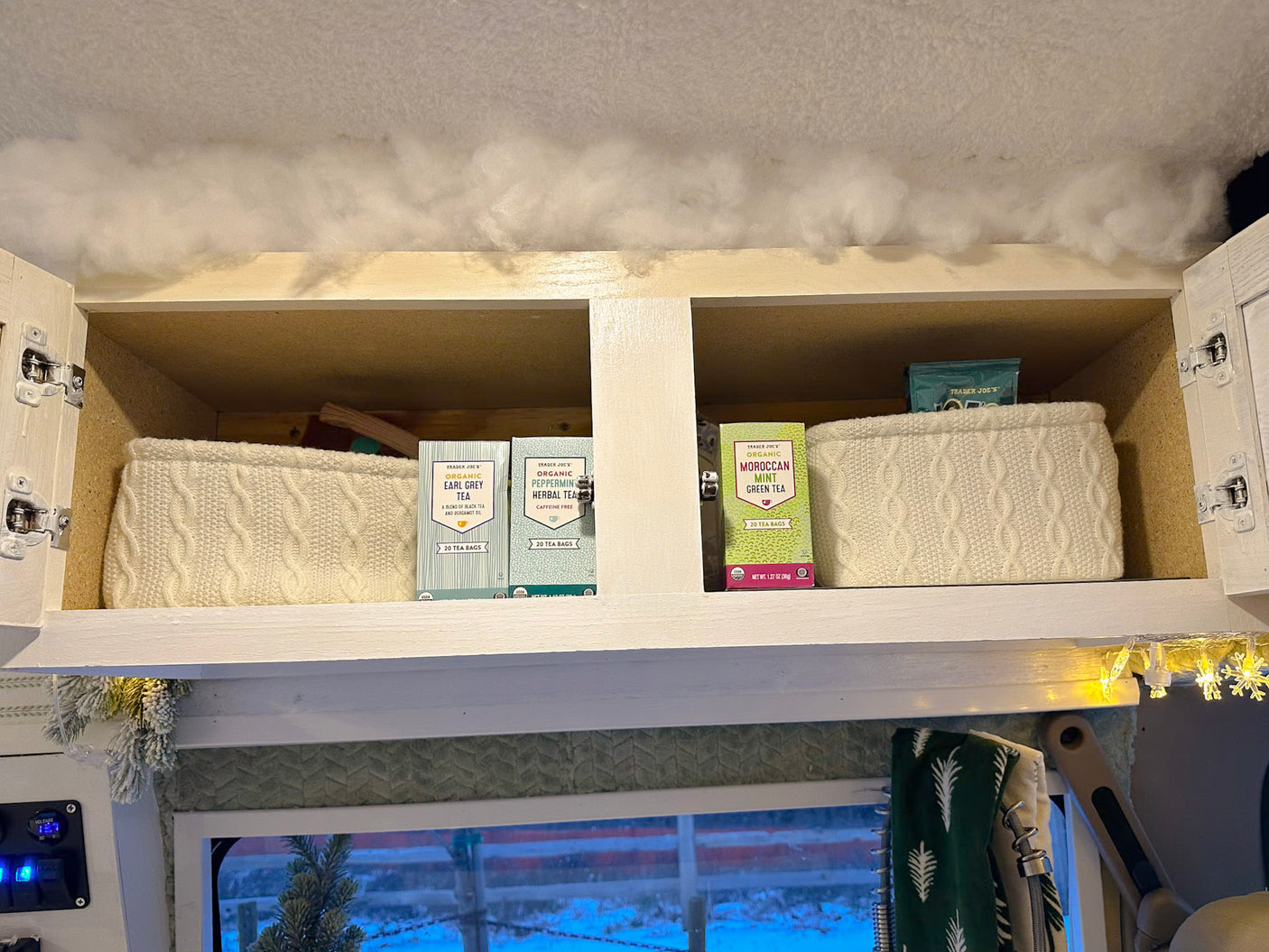 An RV rental's overhead storage showcases organized Trader Joe's teas in cozy cable-knit baskets, ready for winter.