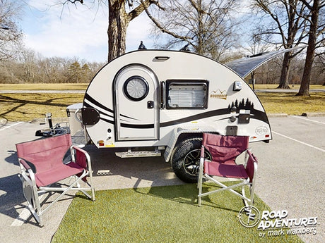 A compact teardrop camper rv rental with an open hatch, camp chairs, and mat, ready for a cozy outdoor adventure.