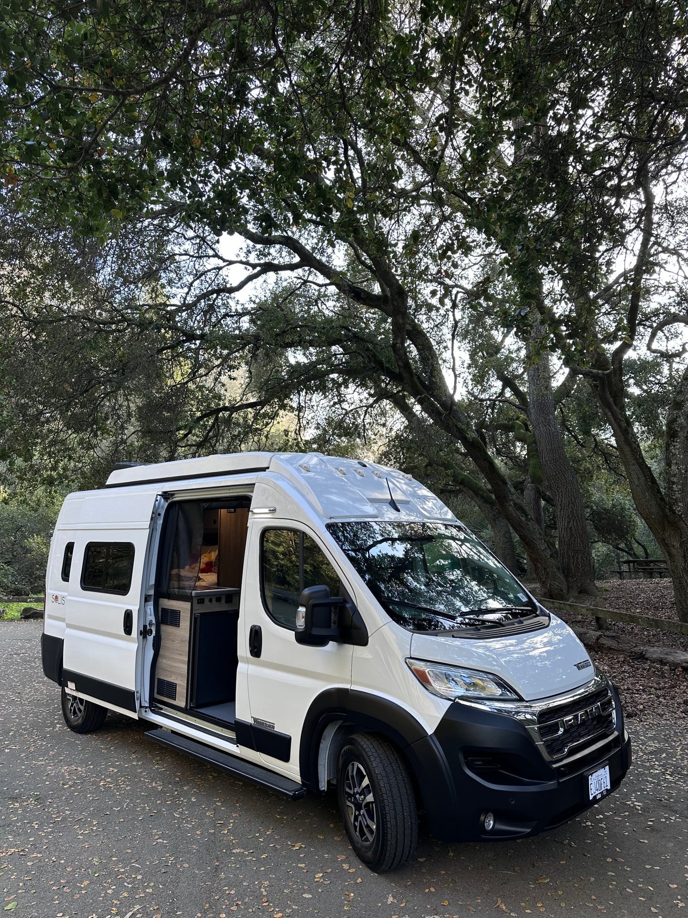  with its pop-top roof raised and side door open revealing the interior.|White Winnebago Solis RV rental with side door open — photo 2