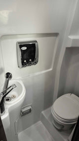 Compact RV rental bathroom with white sink, chrome faucet, wall-mounted dispenser, and toilet. Efficient use of space.