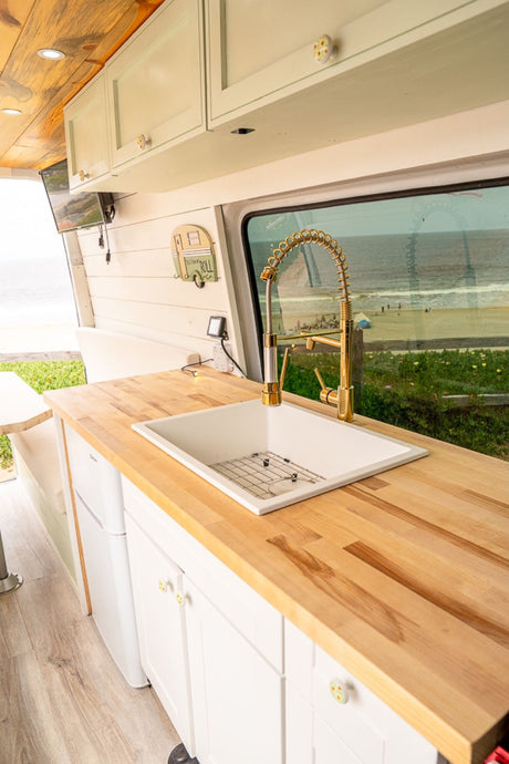 This RV rental camper van boasts a bright kitchen with a golden faucet, wood counters, and a stunning beach view.