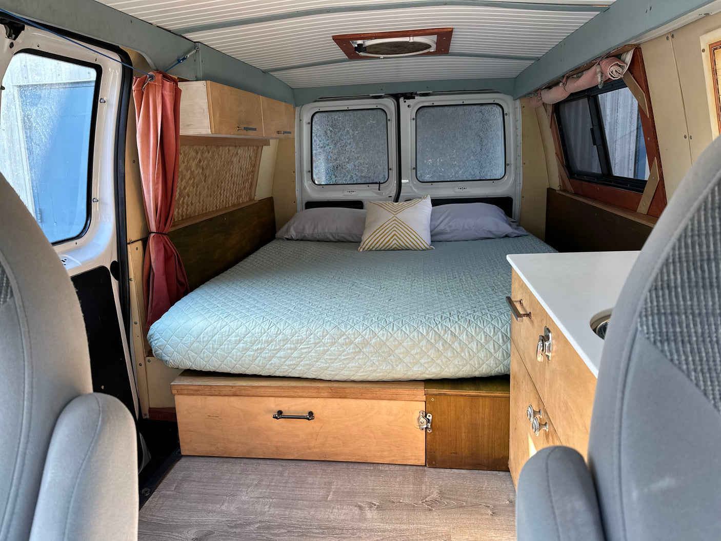 Inside a cozy rv rental camper van with a large bed, built-in storage, and small kitchen area.