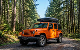 Orange Jeep Wrangler with a rooftop tent on a forest road, an ideal rv rental for off-road camping adventures.