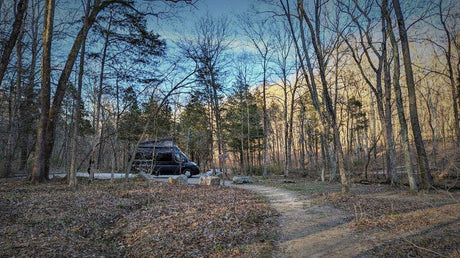 Black RV rental parked on a dirt path in a bare winter forest. Ideal for secluded camping trips.