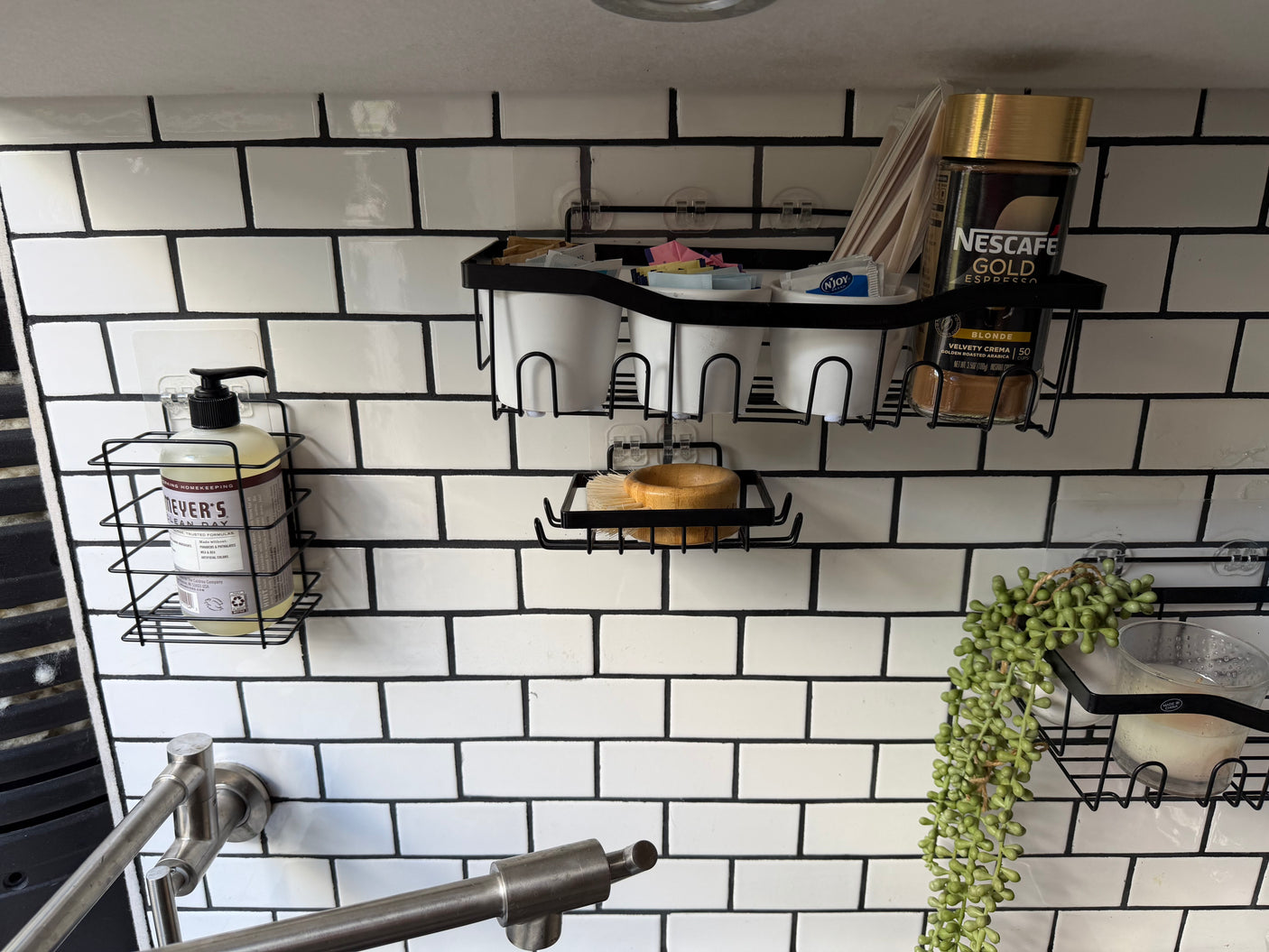 RV rental kitchen: space-saving wall organizers hold dish soap, coffee, cups, and a plant against white subway tiles.