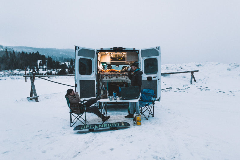 Winter RV rental adventure: Two people relax outside a camper van in snowy mountains; a snowboard lies nearby. — photo 14