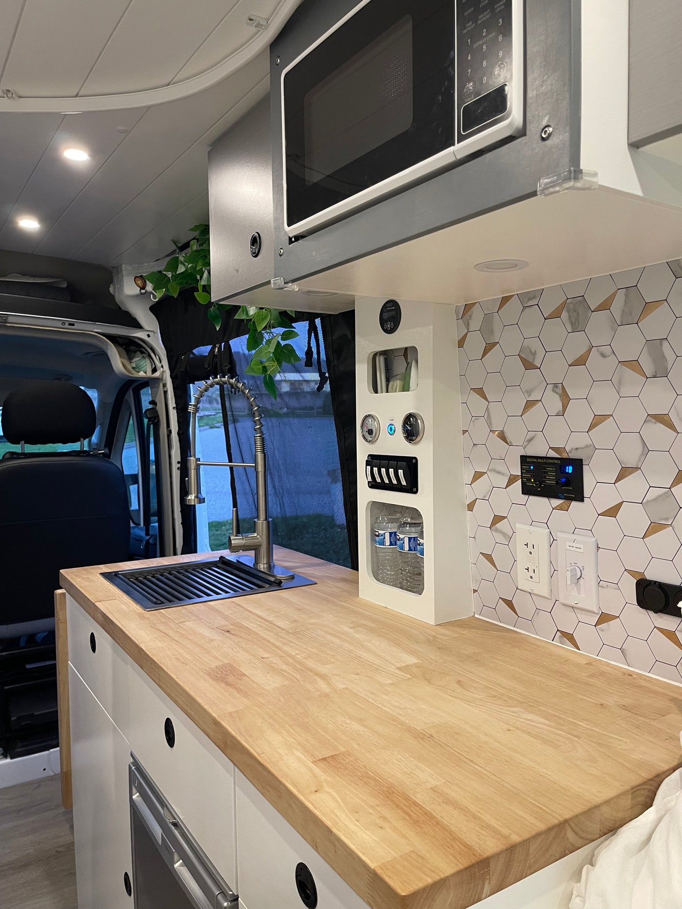 Modern RV rental kitchen with microwave, sink, wood counter, hexagon backsplash, and control panel for on-the-road living.