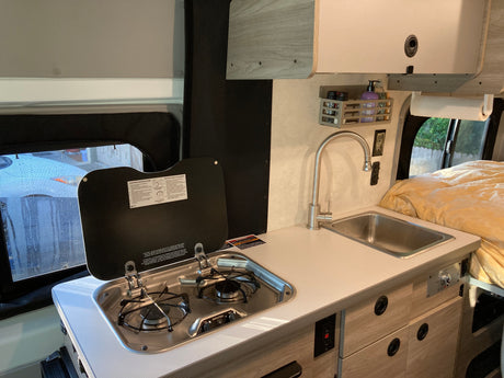 Explore this rv rental's practical interior: a fully-equipped kitchenette with stove, sink, and storage for your adventures.