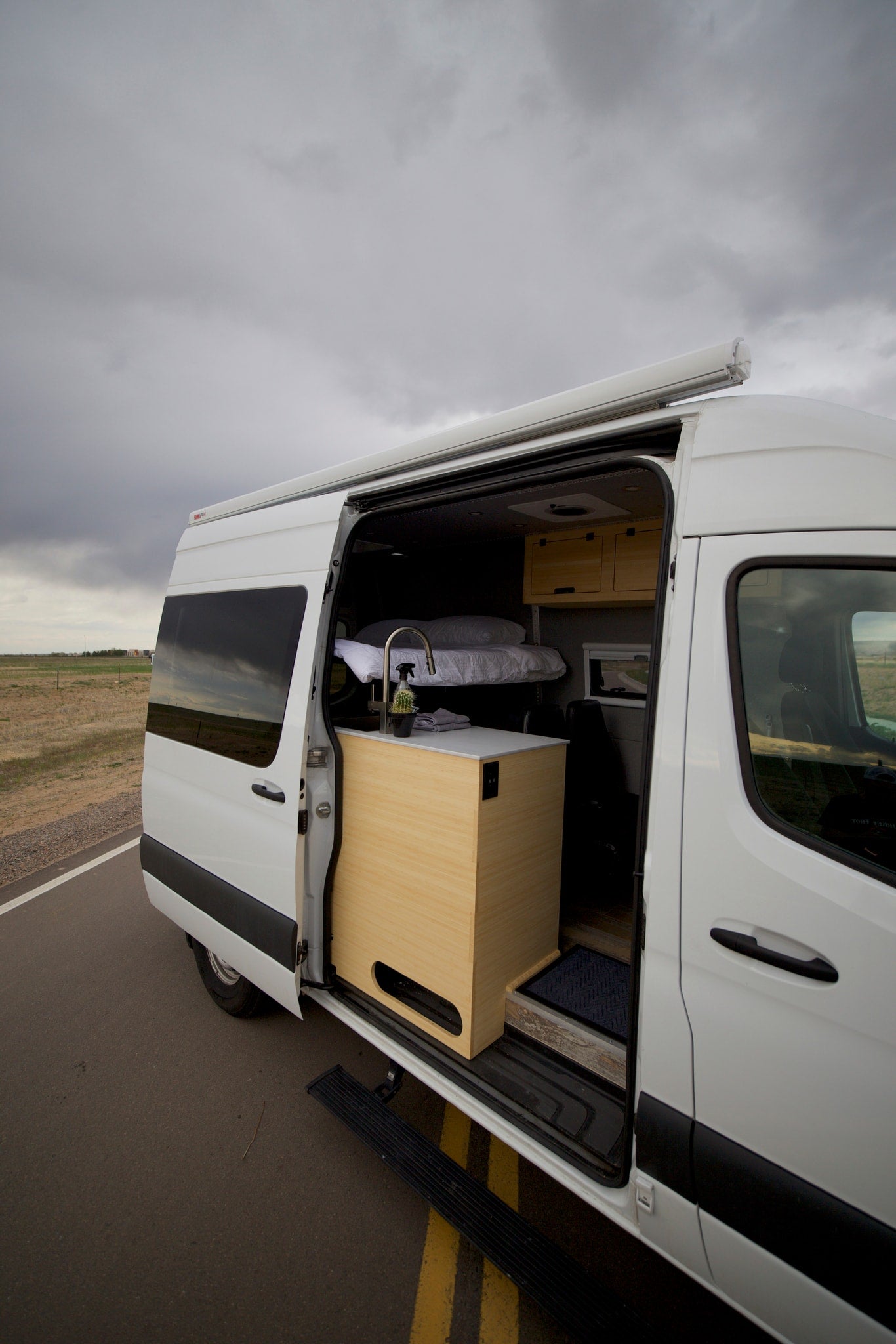  parked on an asphalt road under a cloudy sky.|White camper van with side door open — photo 5