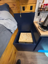 Compact RV rental interior featuring a cozy bed, open storage box, and a functional kitchen area.