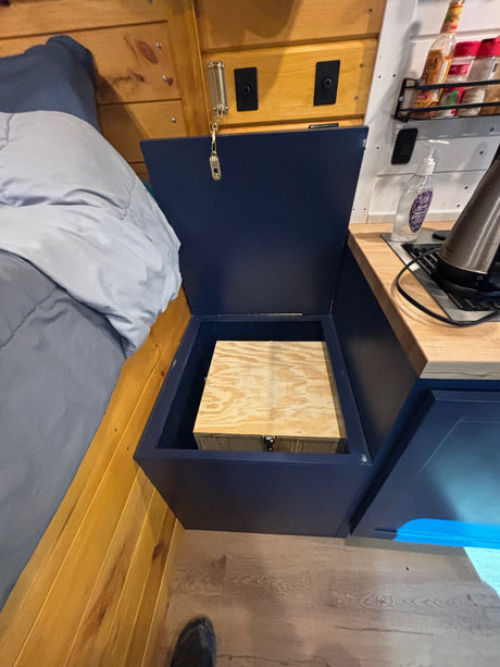 Compact RV rental interior featuring a cozy bed, open storage box, and a functional kitchen area.