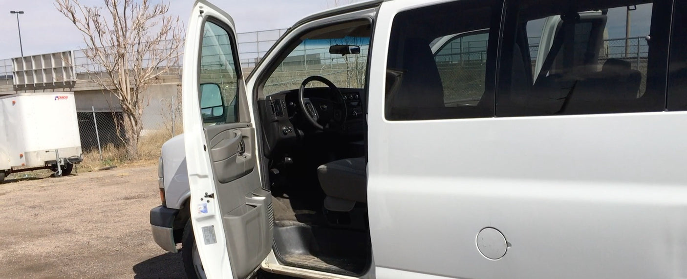White Chevrolet Express-style van for RV rental has its driver's door open, showing the interior.