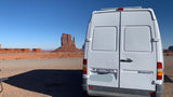 An RV rental Sprinter van at iconic Monument Valley, showcasing towering red rock formations under a clear sky.