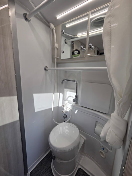Compact and functional RV rental bathroom, featuring a toilet, shower, and mirrored cabinet for convenient travel.