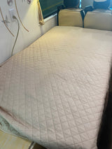 RV rental bed with a quilted cover, showing the interior with an outlet and front seats.