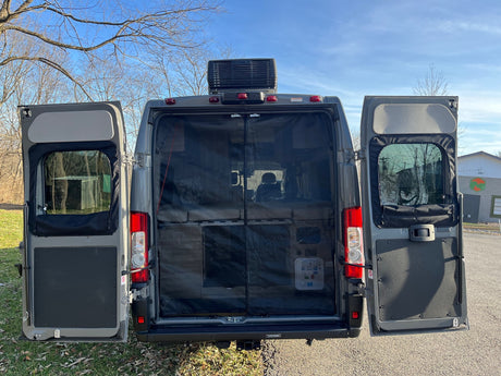 This RV rental van's rear doors are open, revealing a bug screen, interior bed, and a rooftop AC unit under a blue sky.