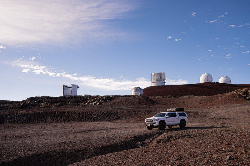 White Toyota Tacoma RV rental exploring Mauna Kea's volcanic landscape near observatories under a bright sky. — photo 8