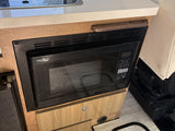 This RV rental features a built-in HIGH POINTE microwave, seamlessly integrated into the wood cabinetry for convenient cooking on the go.