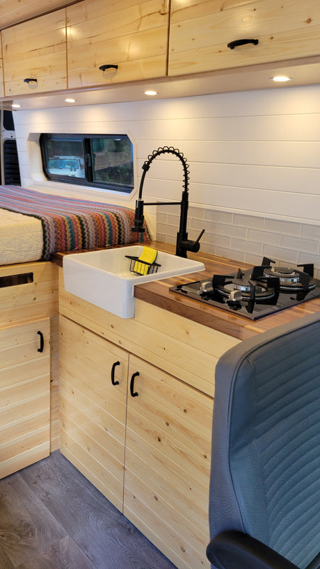 This cozy RV rental features a bright kitchen with a farmhouse sink, stove, wood counters, and a comfy bed.