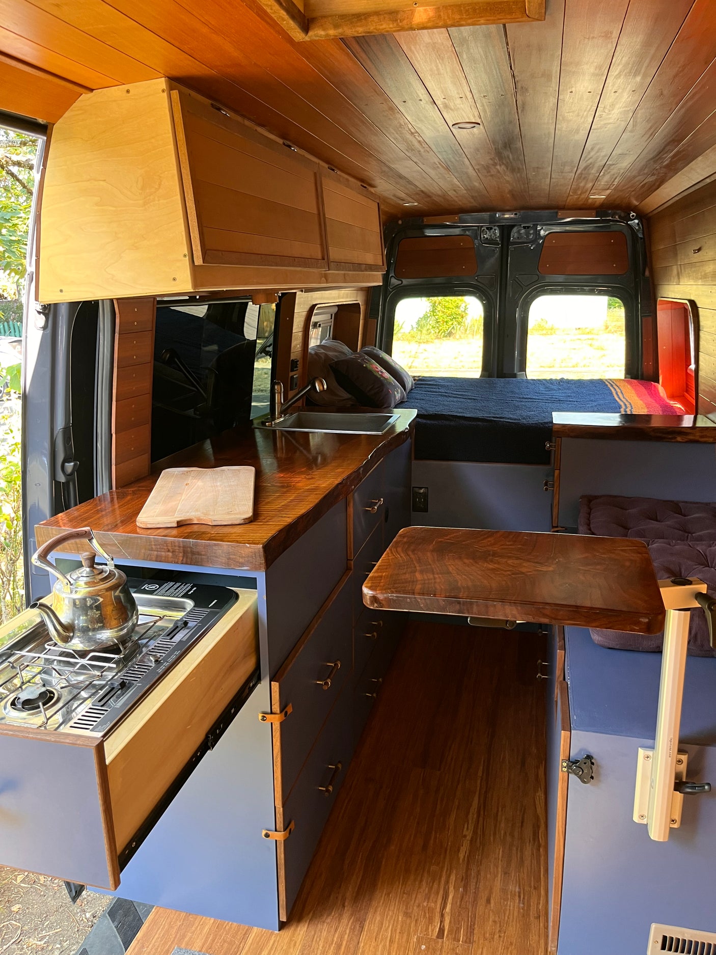 Detailed RV rental interior: rich wood paneling, blue cabinets, compact kitchen with stove, and versatile living area.