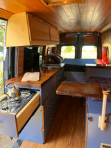 Detailed RV rental interior: rich wood paneling, blue cabinets, compact kitchen with stove, and versatile living area.