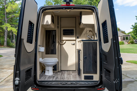 Interior of an RV rental: open rear doors reveal a camper van's compact kitchen, toilet, and storage inside.