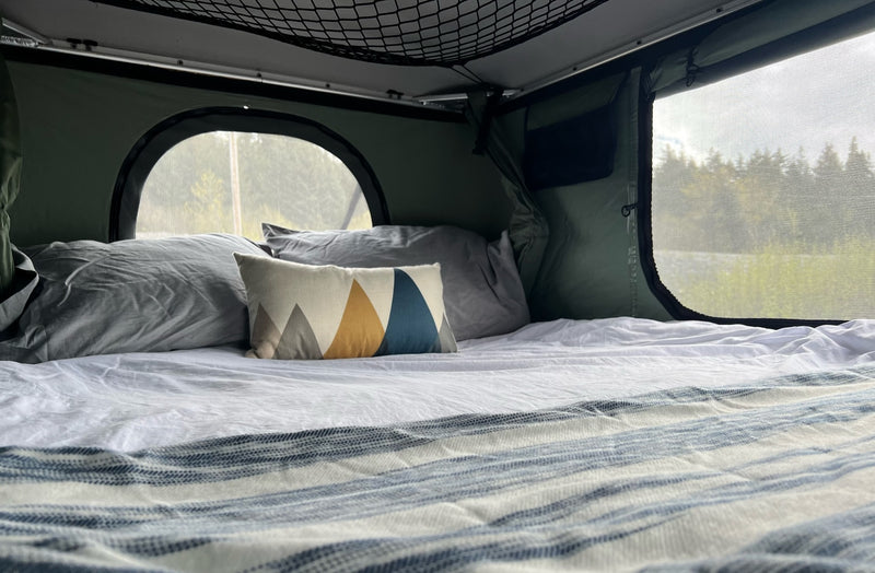 Relax in this RV rental! A cozy bed with fresh linens & mountain pillow offers views through mesh windows to the trees. — photo 8