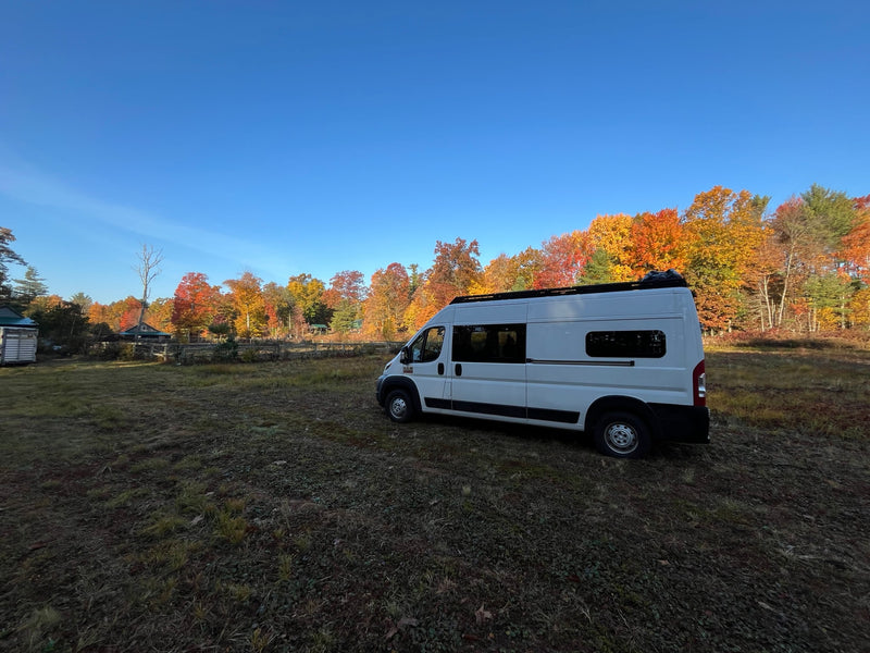 White RV rental parked on a grassy field against a vibrant autumn forest and clear blue sky, ideal for nature getaways. — photo 1