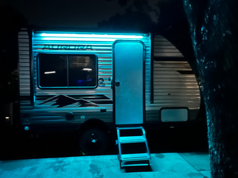 An rv rental brightly lit at night with glowing blue awning lights, an open door, and accessible entry steps on a paved surface. — photo 4