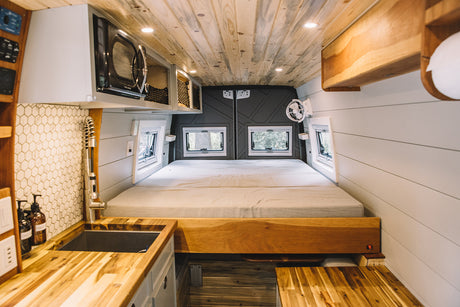 RV rental interior: A cozy camper van with a spacious bed, modern kitchen, and wooden accents throughout.