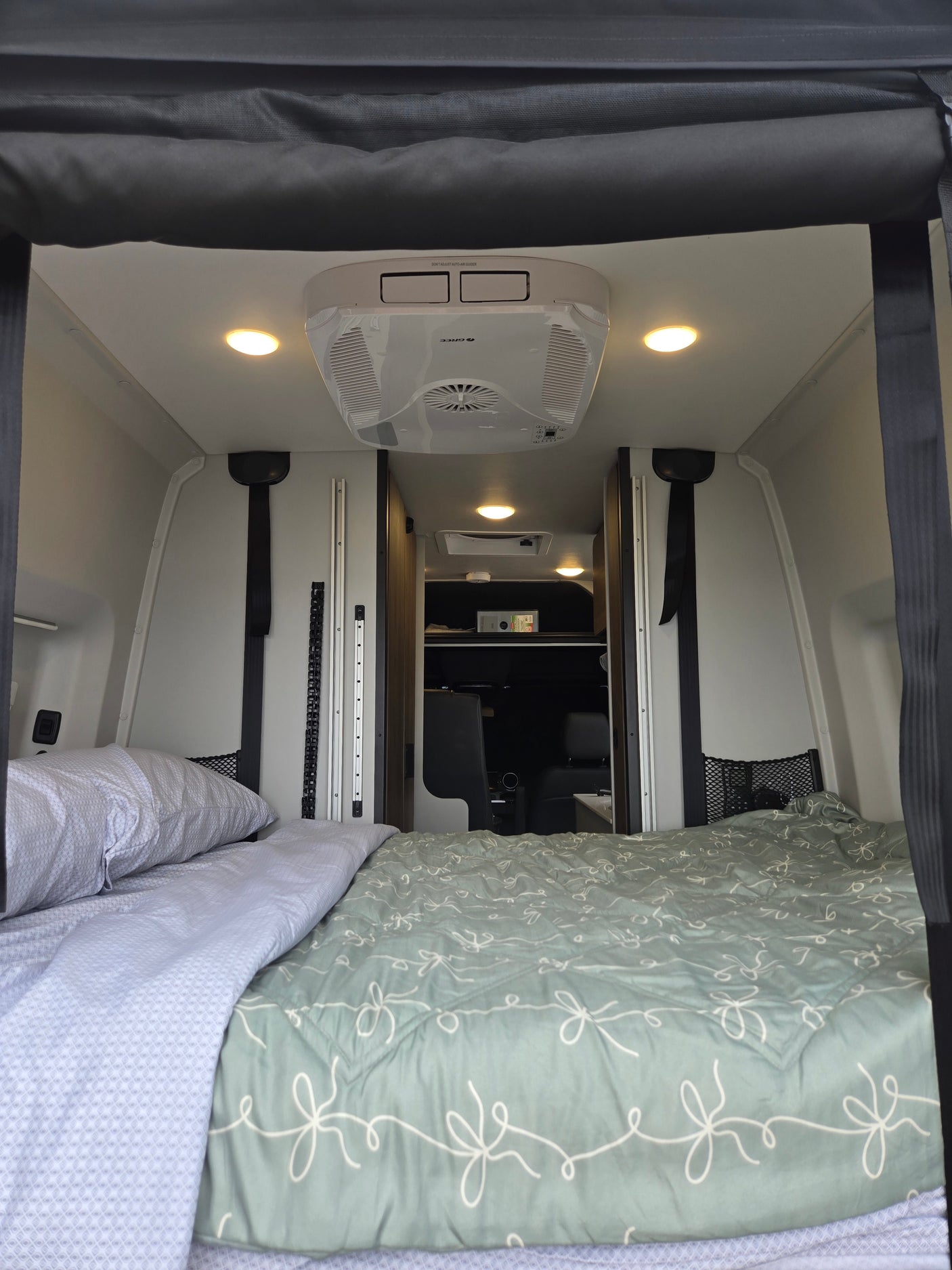 Cozy RV rental interior with a comfortable bed, overhead AC unit, and bright lighting, perfect for compact travel.