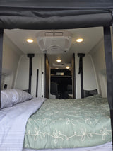 Cozy RV rental interior with a comfortable bed, overhead AC unit, and bright lighting, perfect for compact travel.