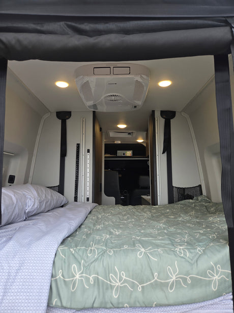Cozy RV rental interior with a comfortable bed, overhead AC unit, and bright lighting, perfect for compact travel.