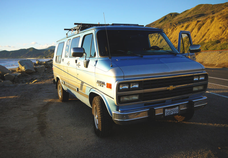 Blue Chevy van parked at a scenic California coast, ideal for an RV rental. Mountains and beach in golden light. — photo 8