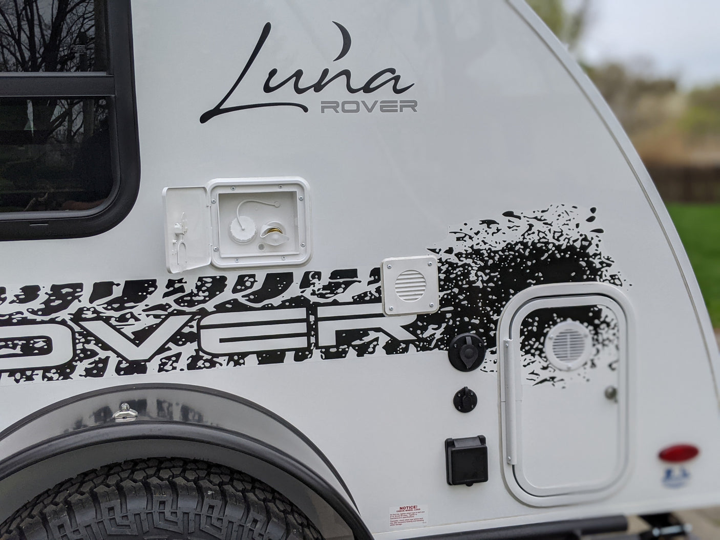 Side view of a white Luna Rover RV rental, showcasing its branding, utility hookups, and durable tire.