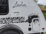 Side view of a white Luna Rover RV rental, showcasing its branding, utility hookups, and durable tire.