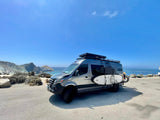 Coastal adventure awaits! Modern rv rental camper van with surfboards & bike overlooking the ocean.