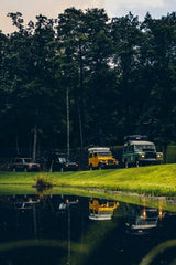 Classic off-road vehicles by a calm pond, their reflections visible. Ideal for adventure, these can be a great RV rental alternative.