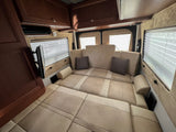 Spacious RV rental interior with a beige bed/lounge area, windows with blinds, and a mounted TV.