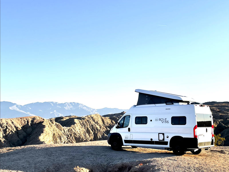 White RV rental van with pop-top roof atop a desert hill, overlooking rugged mountains under a clear sky. — photo 13