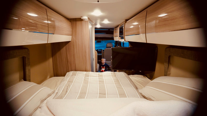 Cozy RV rental interior: A happy child stands near the front, framed by a bed, sleek cabinets, and a mounted TV. Ideal for family road trips. — photo 2
