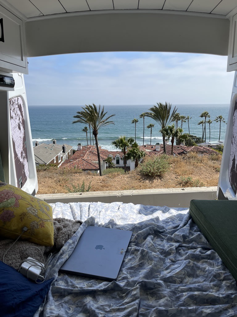 Stunning ocean & palm tree views from a comfy RV rental. Laptop on bed for remote van life, a perfect road trip.