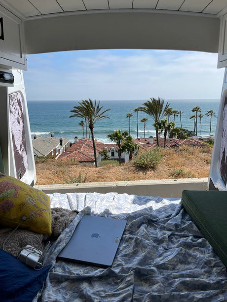Stunning ocean & palm tree views from a comfy RV rental. Laptop on bed for remote van life, a perfect road trip.