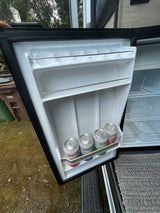 Compact RV rental fridge door open, revealing four Spindrift sparkling waters & inner wire shelves for camping trips.