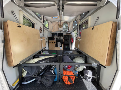 Interior of an rv rental pop-up camper. Beds are lifted, revealing under-bed storage packed with camping gear, alongside a compact kitchen.