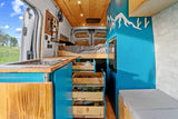 Explore this vibrant rv rental with a fully equipped kitchenette, pull-out storage, comfy bed, and mountain-themed blue interior.