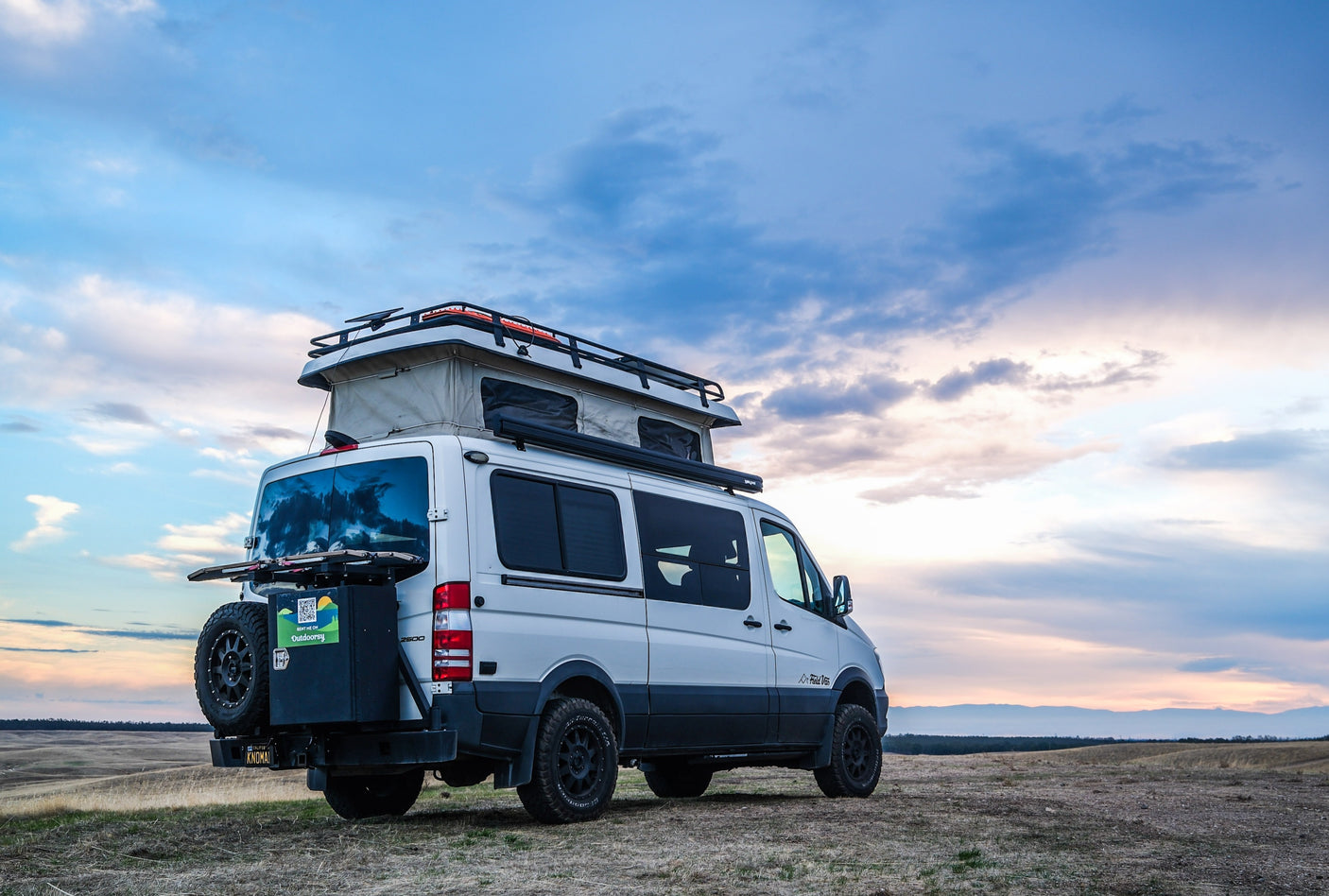 This white pop-top camper van, a perfect RV rental for adventure, is parked on a scenic hill under a beautiful, cloudy sky.