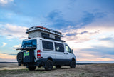 This white pop-top camper van, a perfect RV rental for adventure, is parked on a scenic hill under a beautiful, cloudy sky.